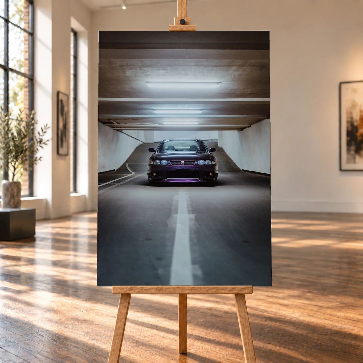 Raumvisualisierung eines hochformatigen Leinwandbilds auf einer Holzstaffelei in einem sonnigen Galerieraum mit großen Fenstern. Auf dem Bild steht ein dunkelvioletter Nissan Skyline GT-R R33 frontal in einer Tiefgarage.