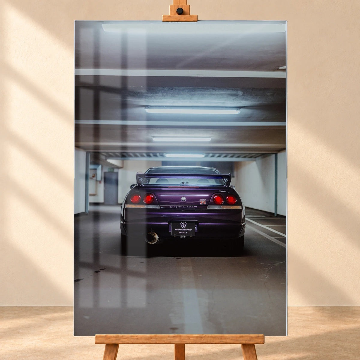 Frontale Visualisierung eines Acrylglasbilds auf einer Holzstaffelei vor beiger Wand. Fensterreflexionen überlagern das Motiv eines violetten Nissan Skyline GT-R R33 V-Spec, dessen Heck mit großem Flügel und roten Rundrückleuchten in einer Tiefgarage zu sehen ist.