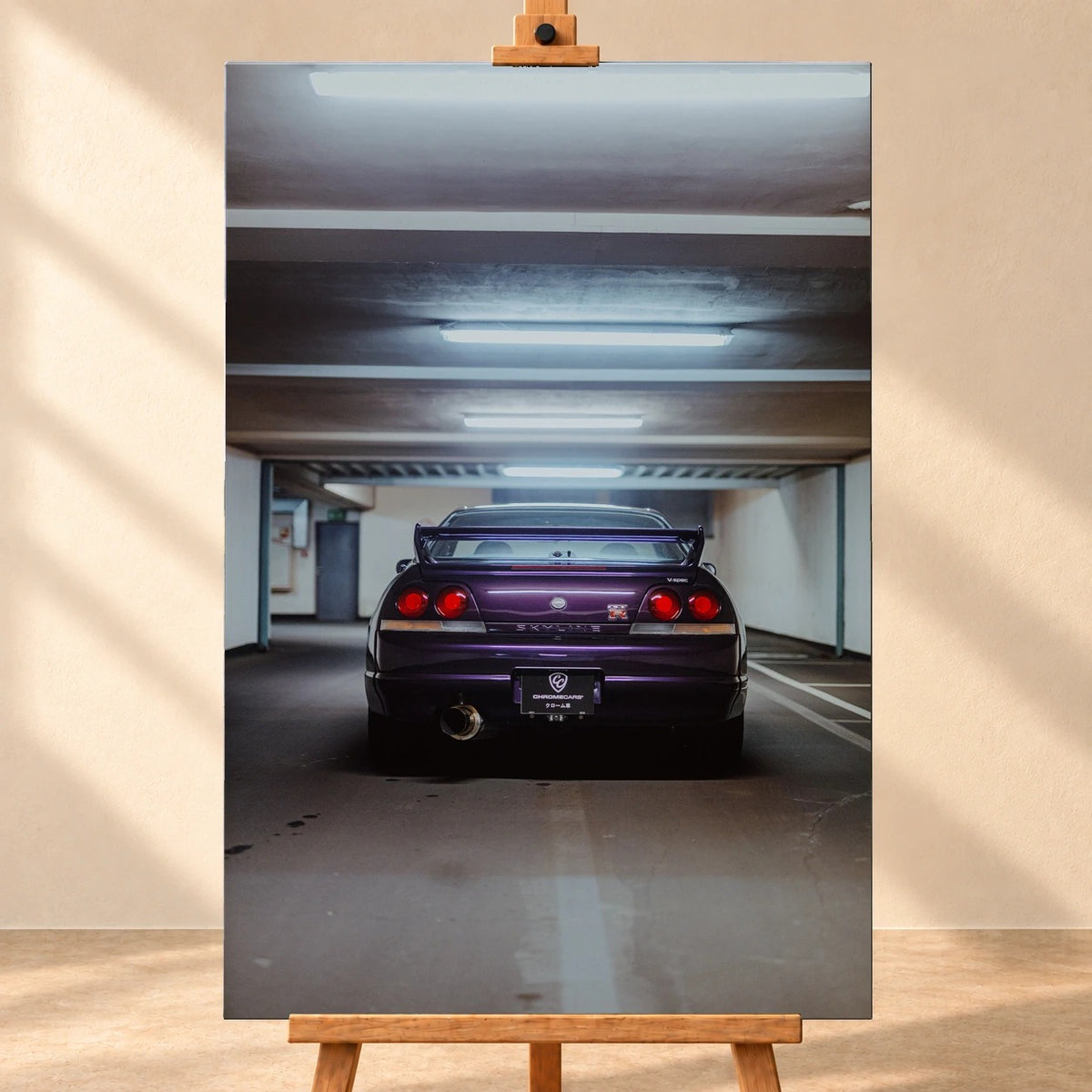 Visualisierung eines hochformatigen Leinwandbilds auf einer Holzstaffelei vor beiger Wand. Das Motiv zeigt einen violetten Nissan Skyline GT-R R33 V-Spec von hinten in einer Tiefgarage, mit Heckflügel und vier runden roten Rückleuchten.