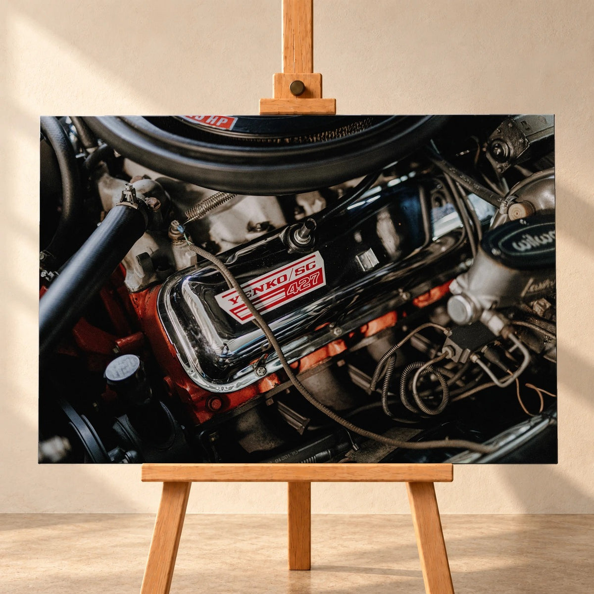 Visualisierung eines querformatigen Leinwandbilds auf einer Holzstaffelei vor heller Wand. Das Motiv zeigt den Motorraum des Chevrolet Camaro Yenko mit dem Schriftzug „YENKO/SC 427“ auf dem verchromten Ventildeckel.