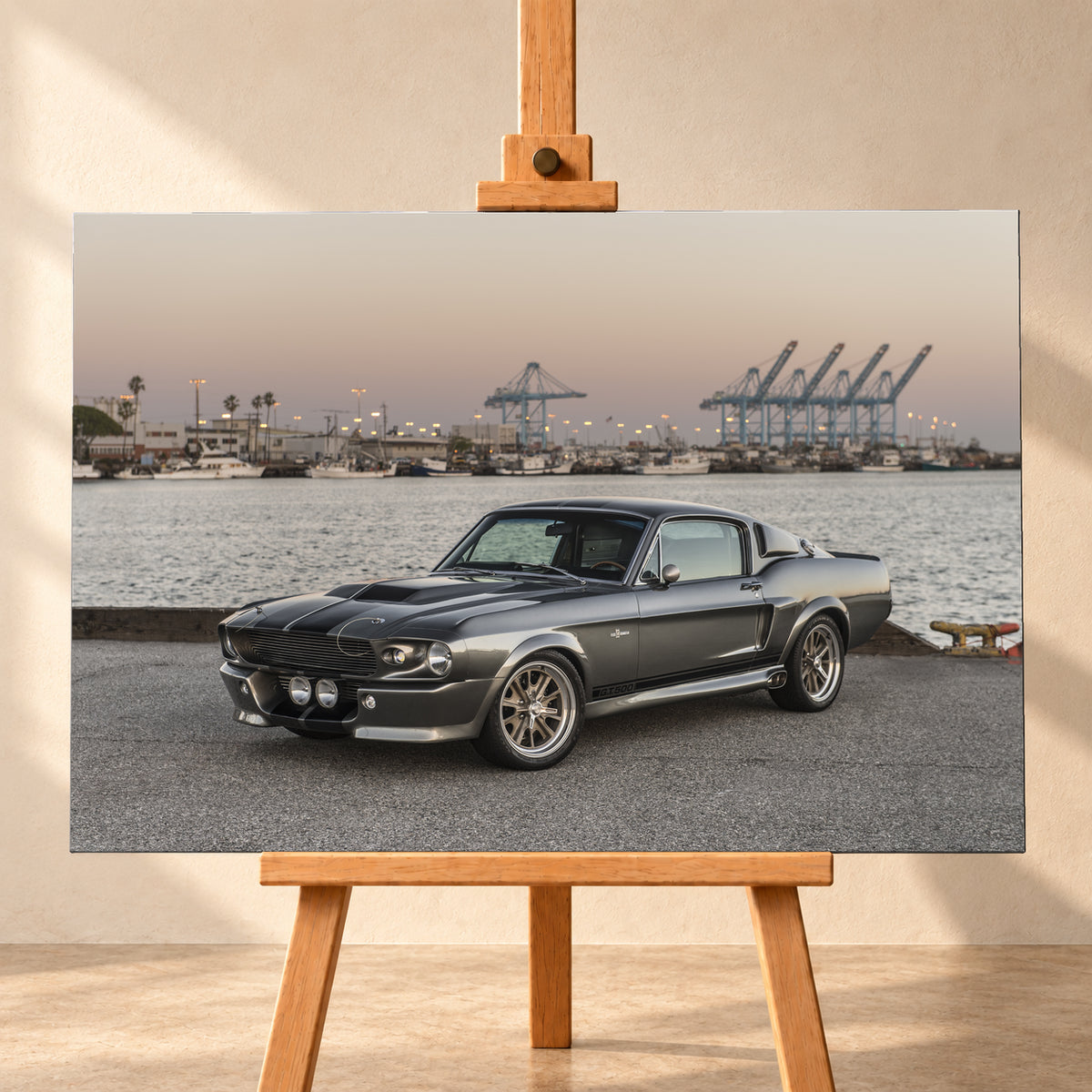 Dunkelgrauer Ford Mustang Shelby GT500 mit kontrastierenden Längsstreifen in Front-Dreiviertelansicht auf einer Hafenfläche; dahinter Wasser, Boote, Containerkräne, leuchtende Hafenlampen und ein pastellfarbener Abendhimmel; Visualisierung als Leinwand-Wandbild, frontal auf einer Holzstaffelei.