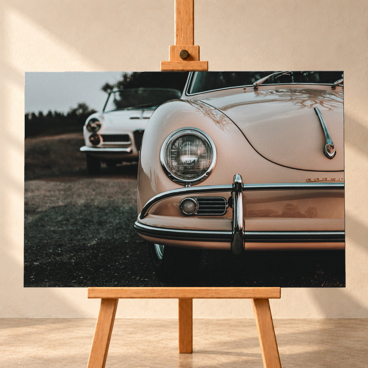 Nahaufnahme der Front eines roséfarbenen Porsche 356 A mit Rundscheinwerfer und Chromstoßfänger rechts; links dahinter steht unscharf ein heller Alfa Romeo 2000 Touring Spider auf dunklem Untergrund unter grauem Himmel; Visualisierung als Leinwand-Wandbild, frontal auf einer Holzstaffelei.