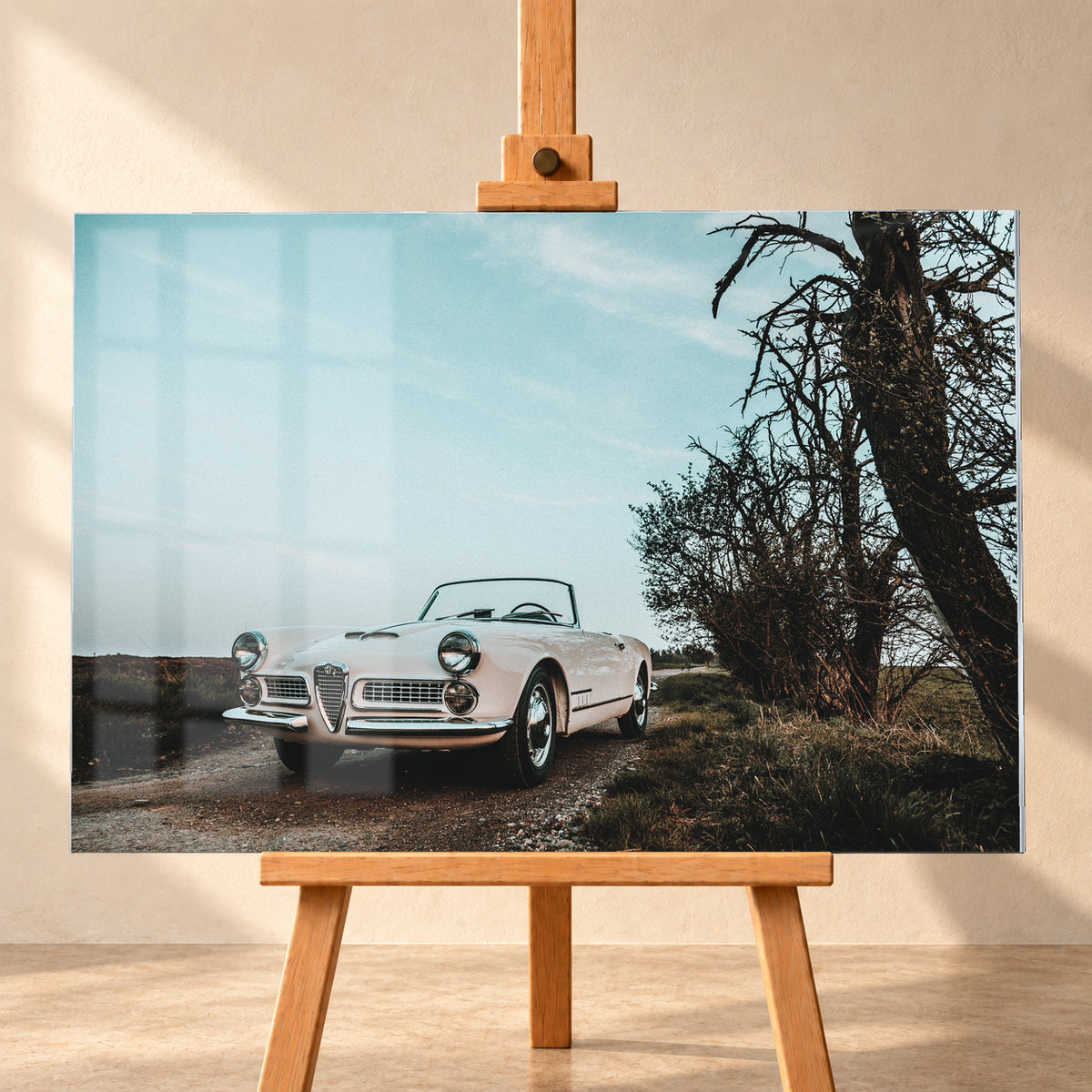 Heller Alfa Romeo 2000 Touring Spider in tiefer Front-Dreiviertelansicht auf einem schmalen Weg neben einem großen knorrigen Baum unter bläulichem, bewölktem Himmel; Visualisierung als Acrylglas-Wandbild, frontal auf einer Holzstaffelei.