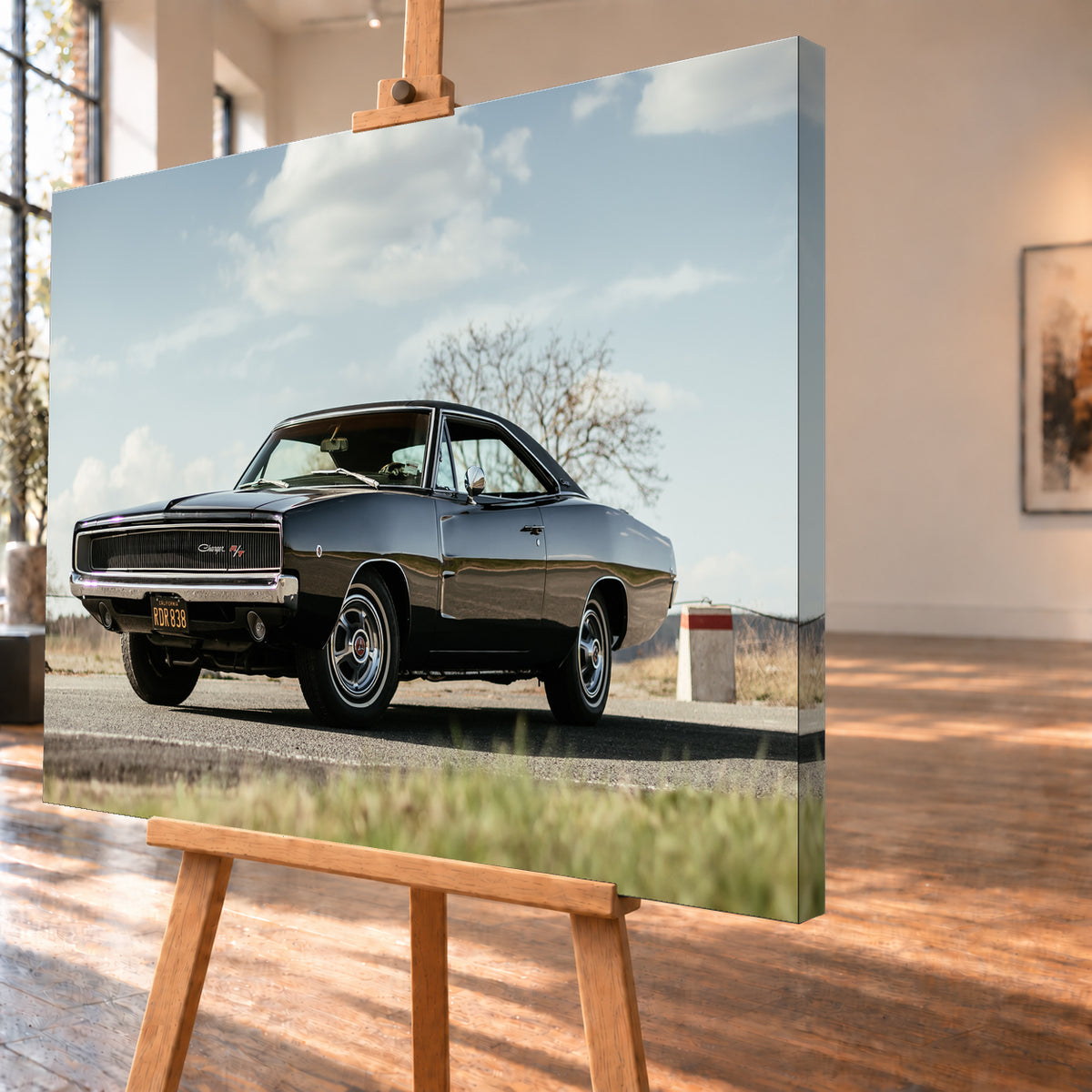 Dunkler Dodge Charger R/T in tiefer Dreiviertelansicht von vorn auf einer Straße unter hellem, wolkigem Himmel; im Hintergrund kahle Bäume und trockenes Gras; Visualisierung als Leinwand-Wandbild, schräg von der Seite auf einer Holzstaffelei.
