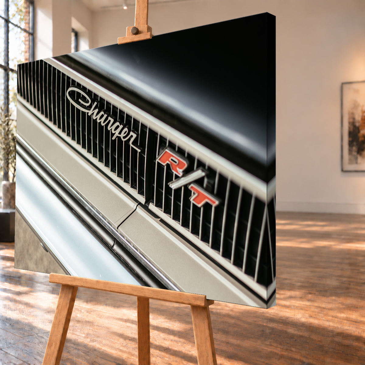 Diagonale Nahaufnahme eines hell lackierten Charger R/T mit schwarzem Lamellengrill, verchromtem Charger-Schriftzug und rot-weißem R/T-Emblem; Chromleisten reflektieren helles Licht; Visualisierung als Leinwand-Wandbild, schräg von der Seite auf einer Holzstaffelei.