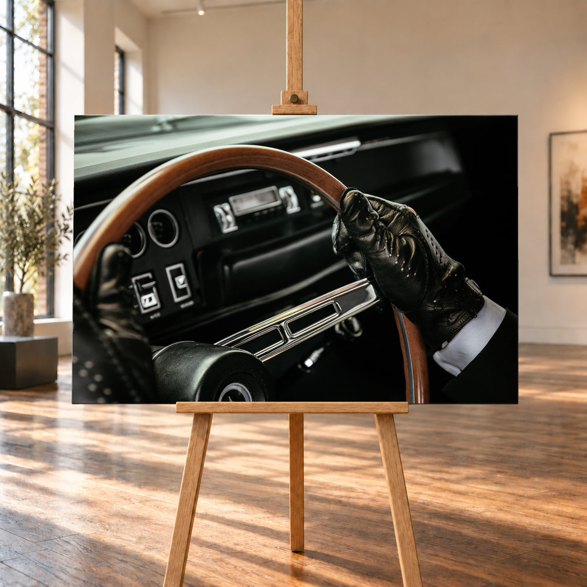 Nahaufnahme eines dunklen Fahrzeugcockpits: Eine Hand in schwarzem, perforiertem Handschuh greift ein braunes, holzfarbenes Lenkrad. Rundinstrumente, Radio und Armaturenbrett liegen unscharf im Hintergrund; seitliches Licht hebt Handschuh, Lenkradkranz und metallisch glänzende Speiche hervor; Visualisierung als Leinwand-Wandbild, auf einer Holzstaffelei in einem hellen Galerieraum.