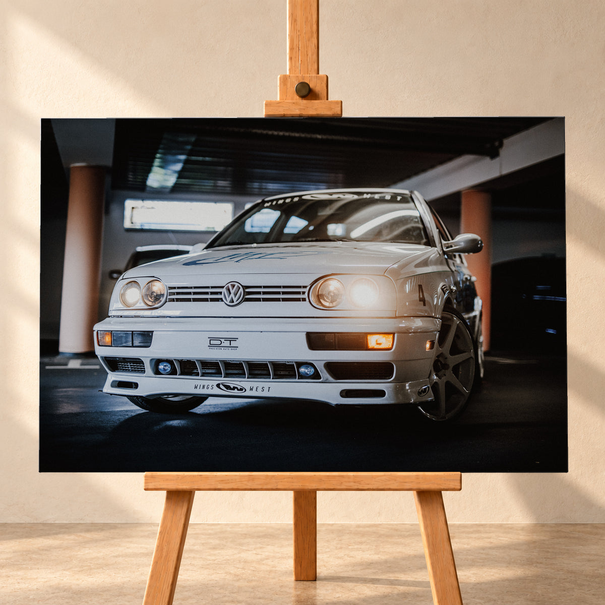 Weißer VW Jetta in niedriger Front-Dreiviertelansicht auf einem dunklen Parkdeck, mit eingeschalteten Scheinwerfern, Dekoren und Startnummer 4. Orangefarbene Säulen, Lichtreflexe und ein unscharfes dunkles Fahrzeug im Hintergrund rahmen die Szene; Visualisierung als Leinwand-Wandbild, frontal auf einer Holzstaffelei.