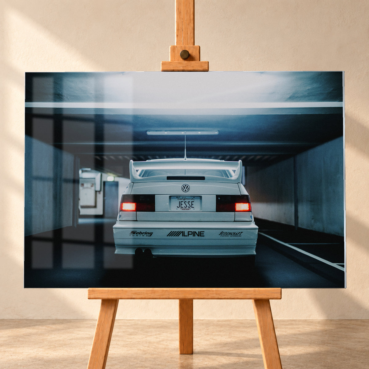 Weißer Volkswagen Jetta in symmetrischer Heckansicht in einer dunklen Betongarage, mit großem Heckflügel, roten Rücklichtern, sichtbaren Aufklebern und kühlem blau-grauem Licht; Visualisierung als Acrylglas-Wandbild, frontal auf einer Holzstaffelei.