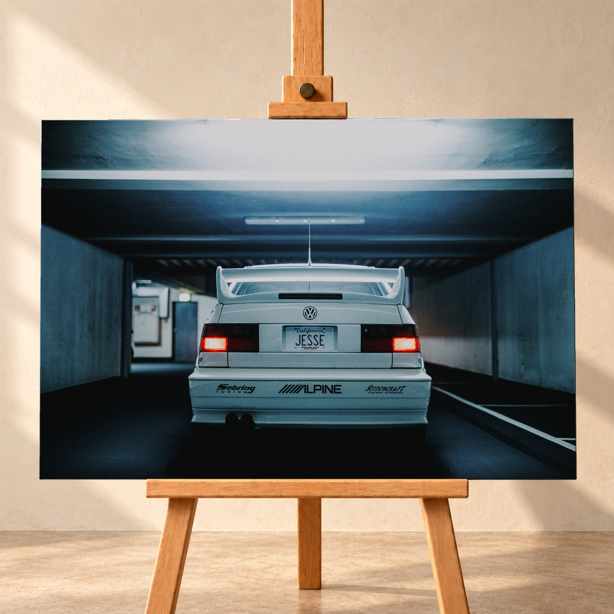 Weißer Volkswagen Jetta in symmetrischer Heckansicht in einer dunklen Betongarage, mit großem Heckflügel, roten Rücklichtern, sichtbaren Aufklebern und kühlem blau-grauem Licht; Visualisierung als Leinwand-Wandbild, frontal auf einer Holzstaffelei.