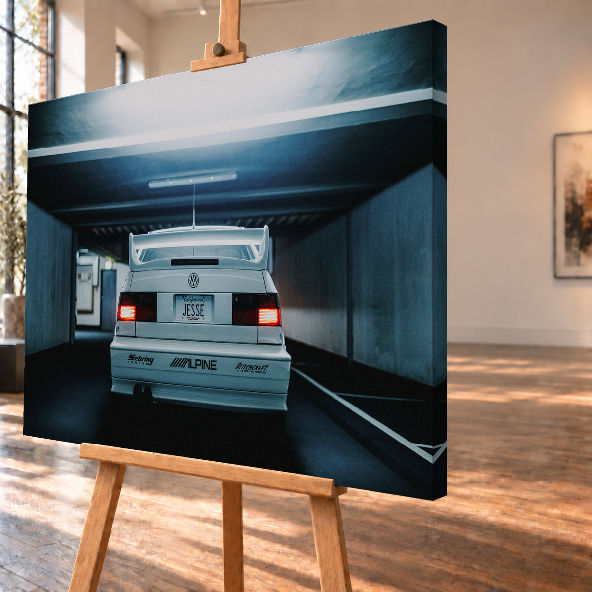 Weißer Volkswagen Jetta in symmetrischer Heckansicht in einer dunklen Betongarage, mit großem Heckflügel, roten Rücklichtern, sichtbaren Aufklebern und kühlem blau-grauem Licht; Visualisierung als Leinwand-Wandbild, schräg von der Seite auf einer Holzstaffelei.