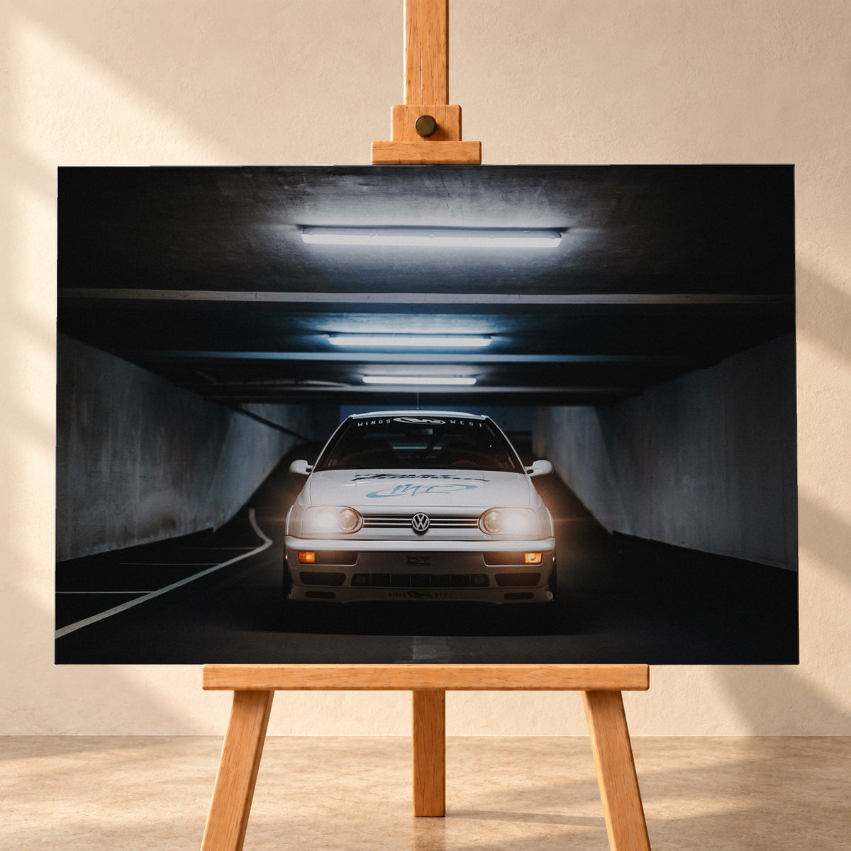 Weißer Volkswagen Jetta in frontaler Ansicht in einer dunklen Betongarage; Scheinwerfer und orangefarbene untere Leuchten sind eingeschaltet, darüber verlaufen helle Deckenröhren; Visualisierung als Leinwand-Wandbild, frontal auf einer Holzstaffelei.