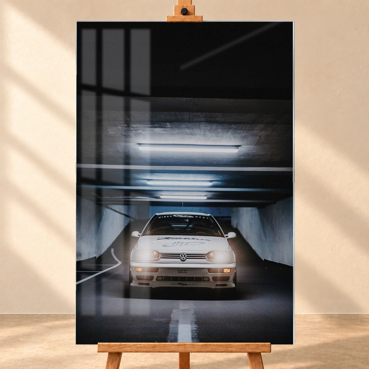 Visualisiertes Acrylglas-Wandbild im Hochformat, frontal auf einer Holzstaffelei vor heller Wand. Fensterreflexionen überlagern das Motiv des weißen VW Jetta aus „The Fast and the Furious“ unter den Deckenleuchten einer Tiefgarage.