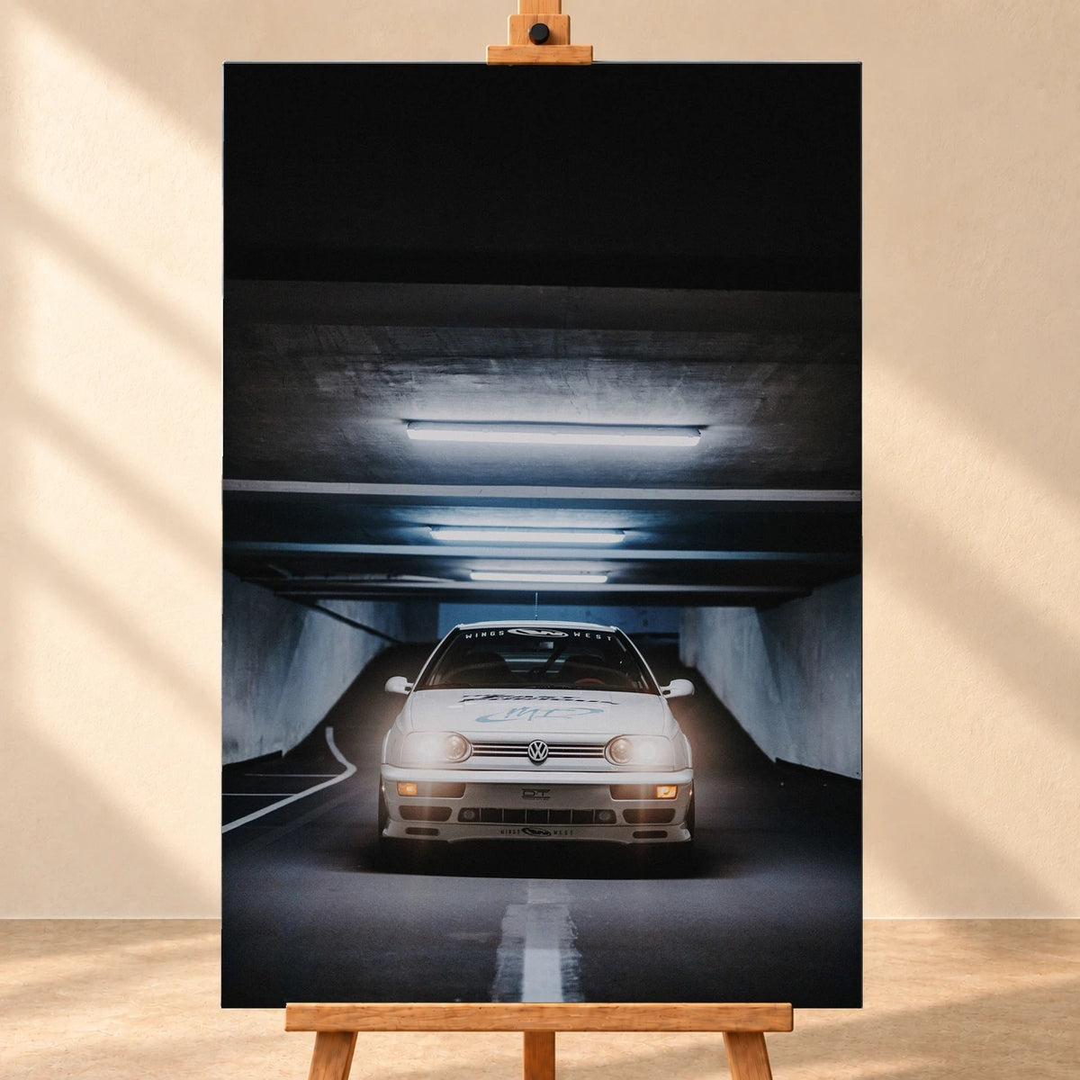 Visualisierung einer hochformatigen Leinwand, frontal auf einer Holzstaffelei vor heller Wand. Das Motiv zeigt den weißen VW Jetta aus „The Fast and the Furious“ in einer dunklen Tiefgarage unter leuchtenden Deckenröhren.