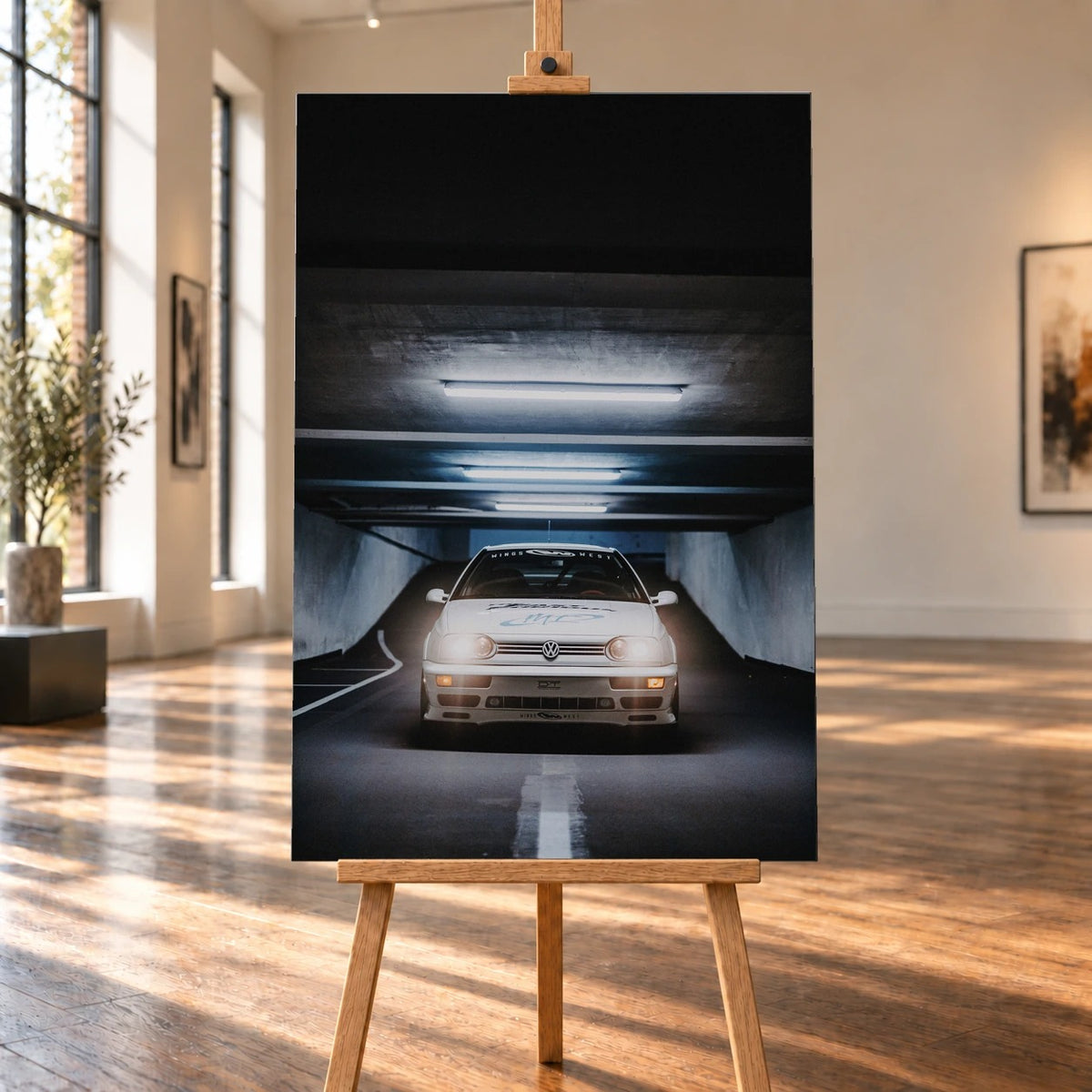 Raumvisualisierung einer hochformatigen Leinwand auf einer Holzstaffelei in einem hellen Raum mit großen Fenstern und Holzboden. Auf der Leinwand erscheint der weiße VW Jetta aus „The Fast and the Furious“ frontal in einer Tiefgarage.
