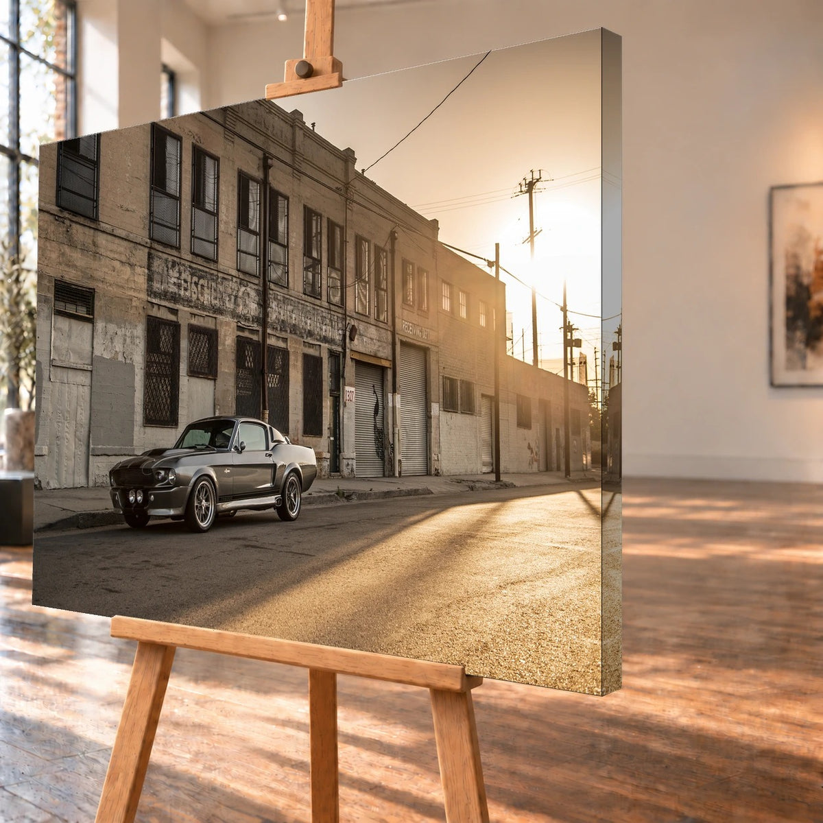 Schrägansicht des Leinwandbilds als Visualisierung auf einer Holzstaffelei, mit über die rechte Seitenkante weitergeführtem Motiv. Mustang „Eleanor“ steht vor alten Industriegebäuden; tief stehende Sonne beleuchtet die Straße von rechts.