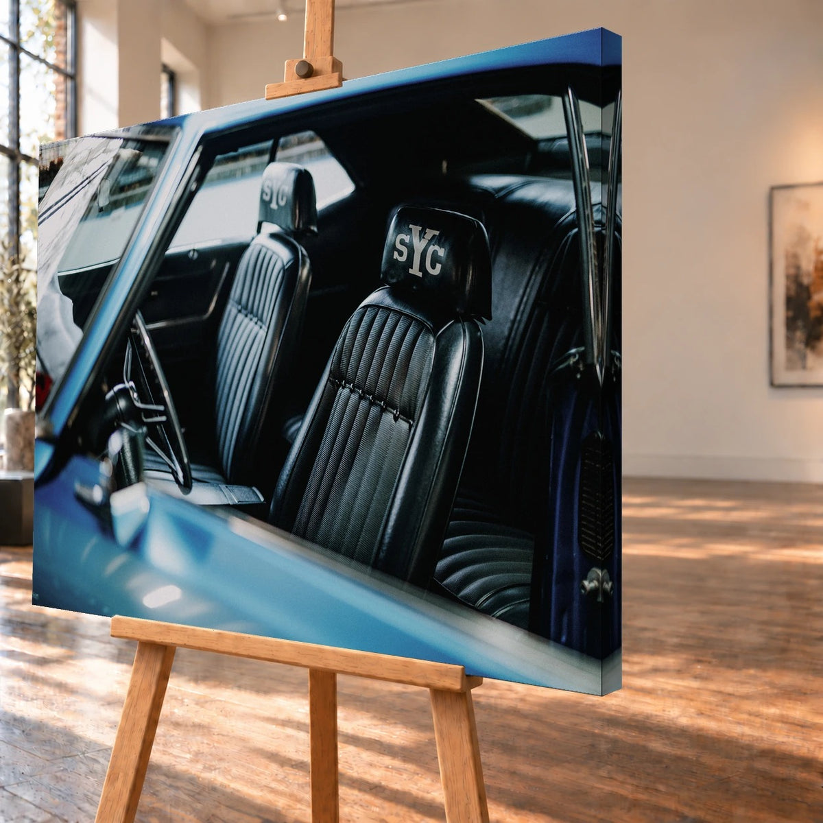 Schrägansicht eines Leinwandbildes als Visualisierung auf einer Holzstaffelei, mit sichtbarer bedruckter rechter Seitenkante. Das Innenraummotiv des blauen Chevrolet Camaro Yenko zeigt schwarze, gerippte Vordersitze mit „sYc“-Schriftzügen auf den Kopfstützen.