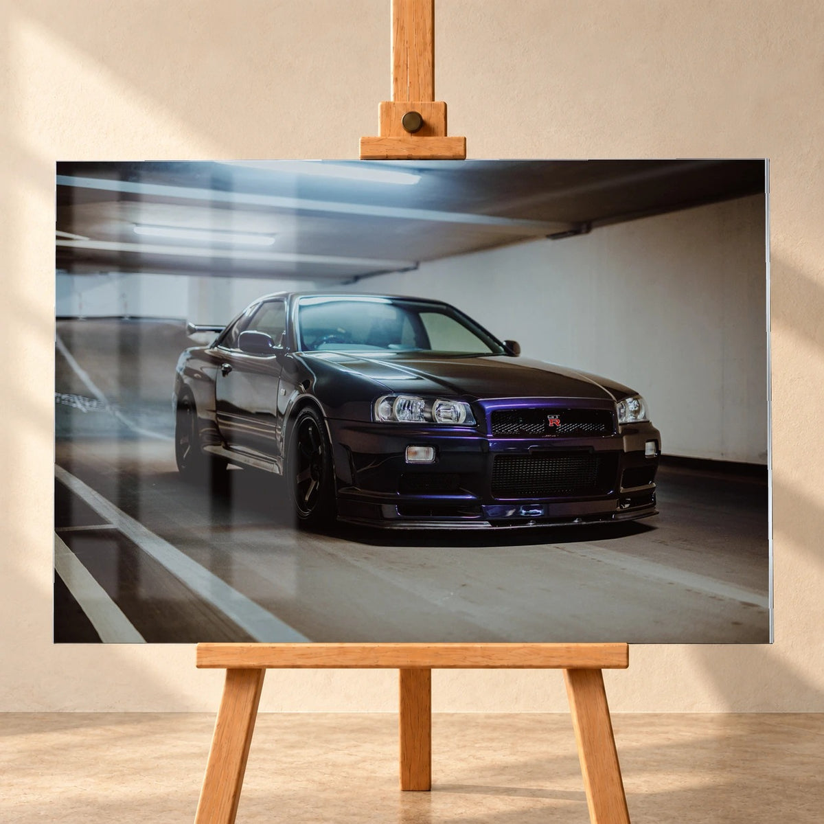 Frontal visualisiertes Acrylglasbild auf einer Holzstaffelei vor heller Wand, mit dargestellten Fensterspiegelungen auf der Bildfläche. Das Motiv zeigt einen dunkelvioletten Nissan Skyline GT-R R34 schräg von vorn in einer Tiefgarage.