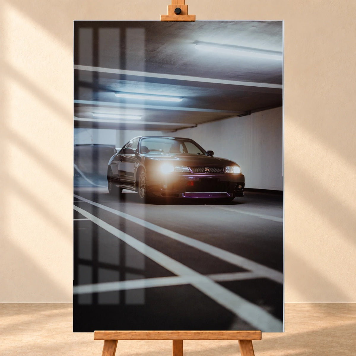 Frontal visualisiertes Acrylglasbild im Hochformat auf einer Holzstaffelei vor heller Wand. Fensterspiegelungen überlagern das Motiv eines dunkelvioletten Nissan Skyline GT-R R33 mit leuchtenden Scheinwerfern in einer Tiefgarage.
