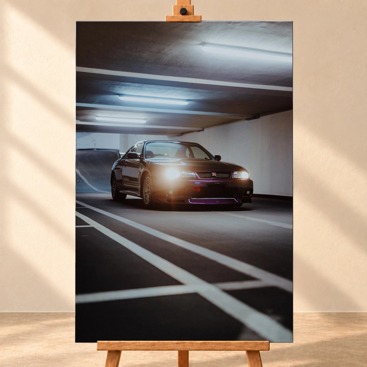 Visualisierung eines hochformatigen Leinwandbildes auf einer Holzstaffelei vor heller Wand. Das Motiv zeigt einen dunkelvioletten Nissan Skyline GT-R R33 mit eingeschalteten Scheinwerfern in einer Tiefgarage.