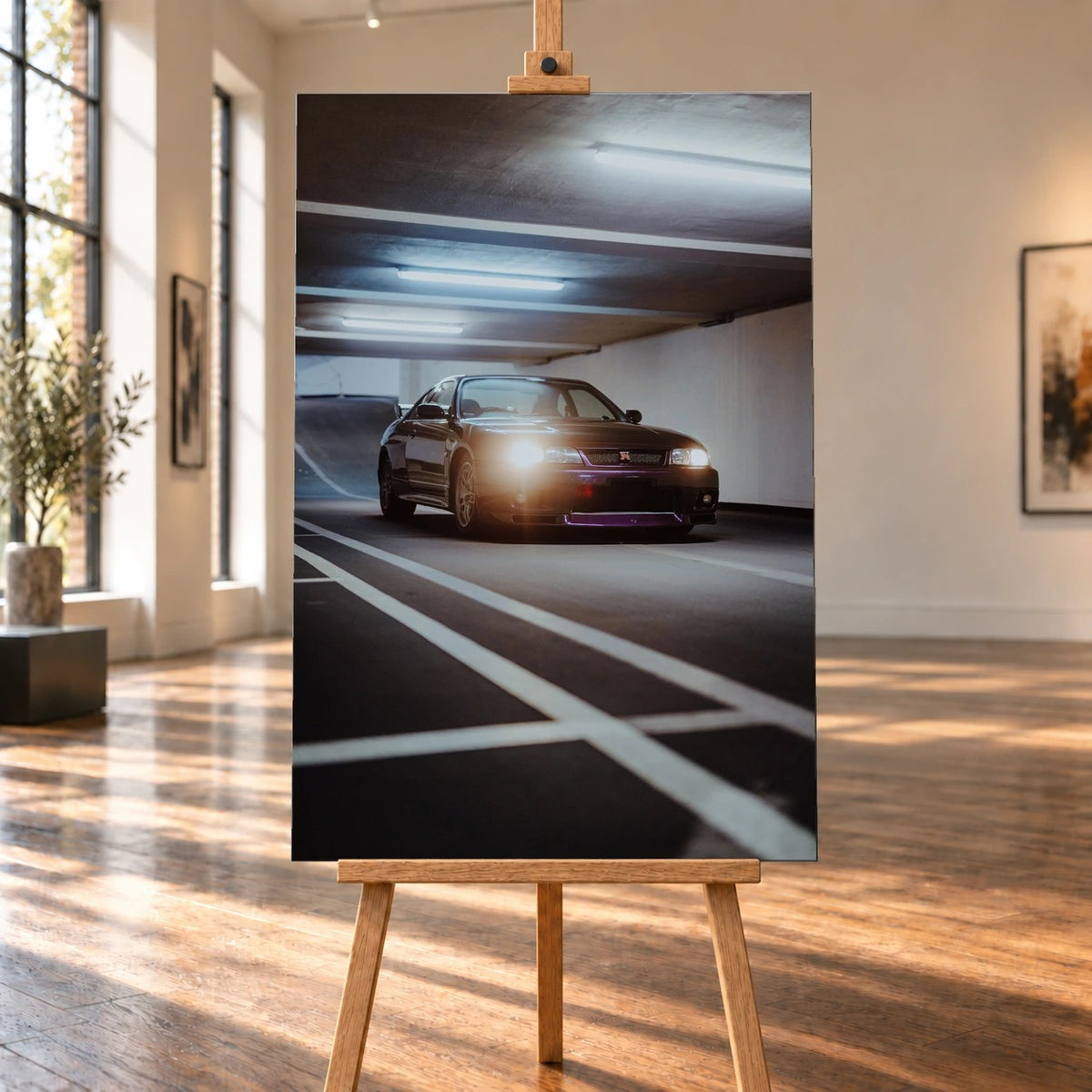 Raumvisualisierung mit einem hochformatigen Leinwandbild auf einer Holzstaffelei in einer sonnigen Galerie mit großen Fenstern und Holzboden. Das Bild zeigt einen Nissan Skyline GT-R R33 mit eingeschalteten Scheinwerfern unter den Deckenleuchten einer Tiefgarage.