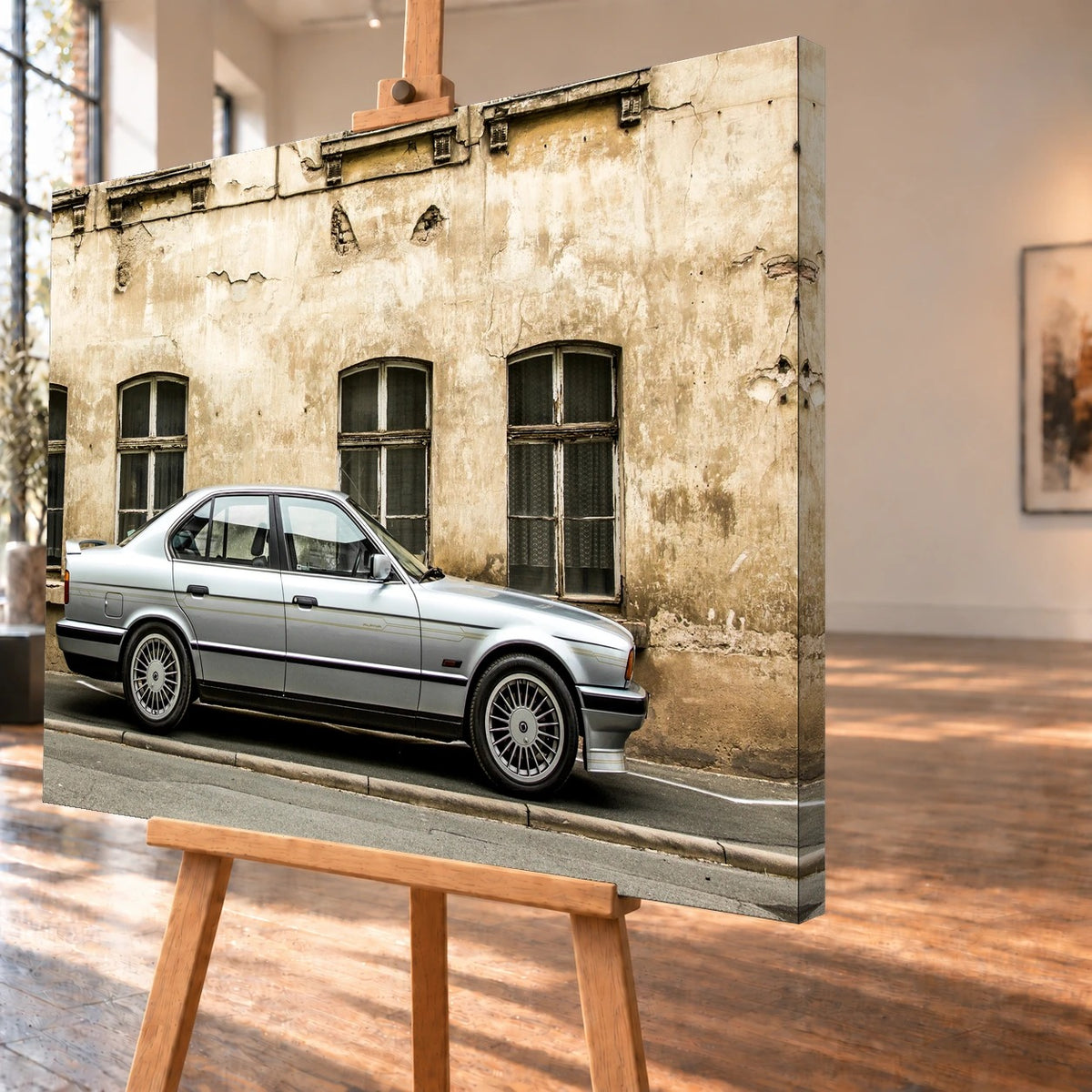Schräge Visualisierung des Leinwandbilds auf einer Holzstaffelei, mit über die rechte Seitenkante fortgeführtem Motiv. Ein silberner BMW Alpina B10 steht mit der Front nach rechts vor einer beigefarbenen Fassade mit abblätterndem Putz.