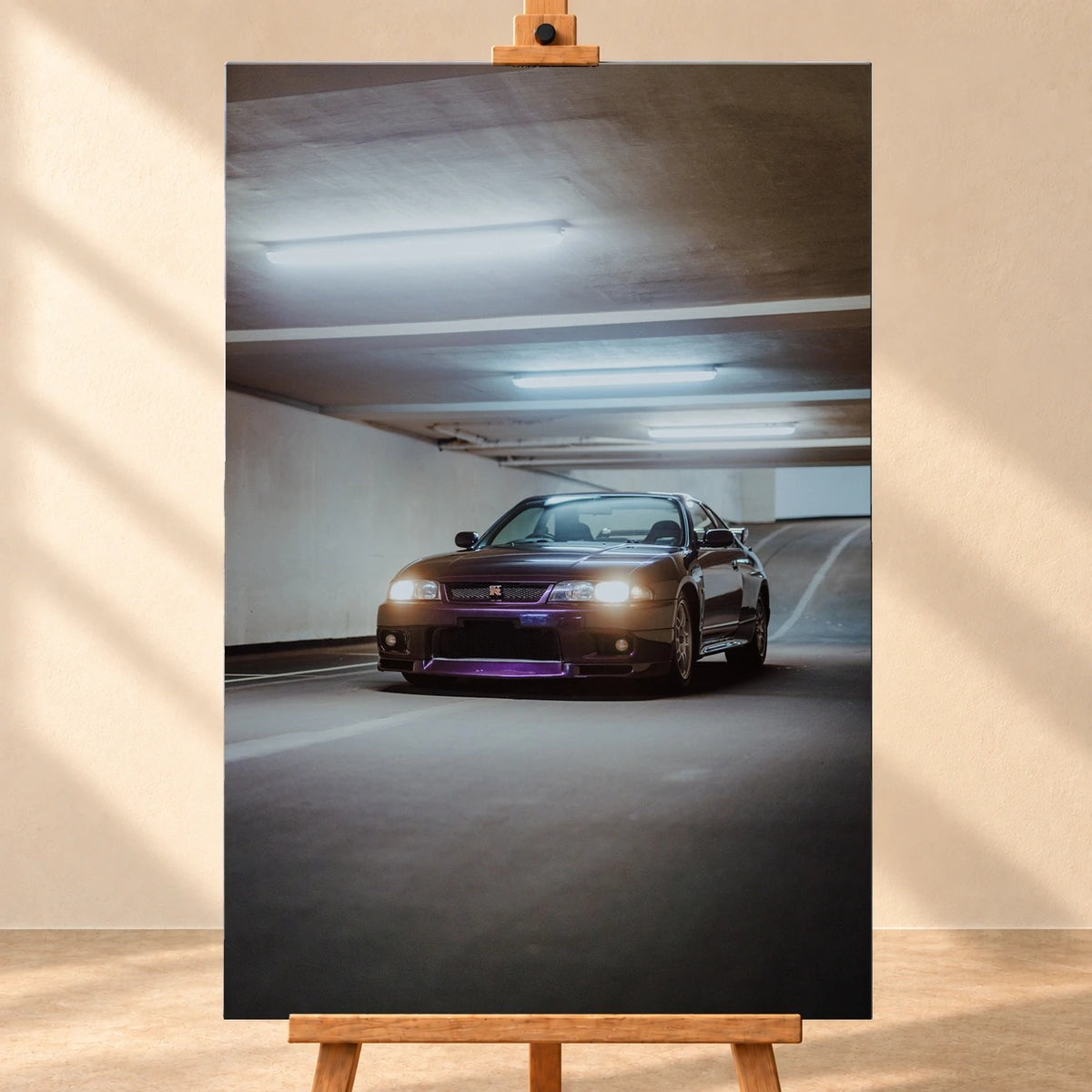 Visualisierung einer hochformatigen Leinwand, frontal auf einer Holzstaffelei vor heller Wand. Das Motiv zeigt einen dunkelvioletten Nissan Skyline GT-R R33 mit eingeschalteten Scheinwerfern, schräg von vorn in einer Tiefgarage.