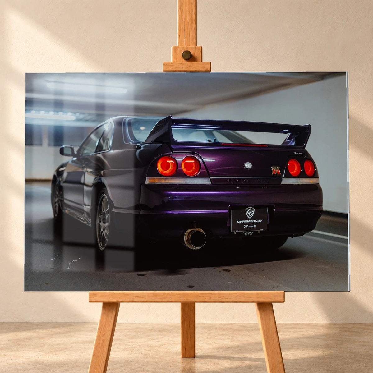 Acrylglas-Wandbild als Visualisierung auf einer Holzstaffelei vor heller Wand. Fensterspiegelungen überlagern links das Motiv eines violetten Nissan Skyline GT-R R33 V-Spec, schräg von hinten mit großem Heckflügel und roten Rückleuchten.