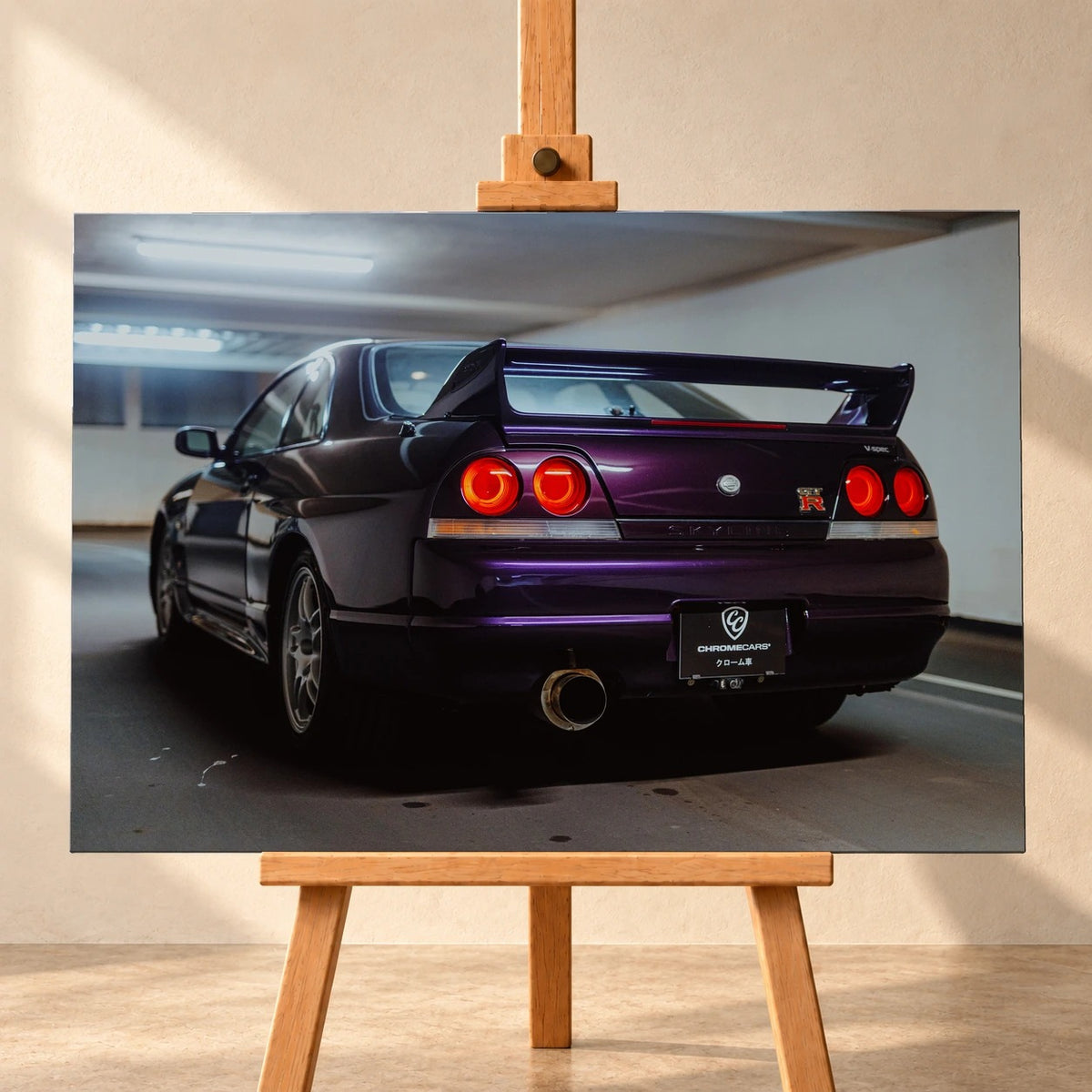 Visualisierung eines querformatigen Leinwandbilds auf einer Holzstaffelei vor heller Wand. Das Motiv zeigt einen violetten Nissan Skyline GT-R R33 V-Spec schräg von hinten mit großem Heckflügel und vier roten Rückleuchten.
