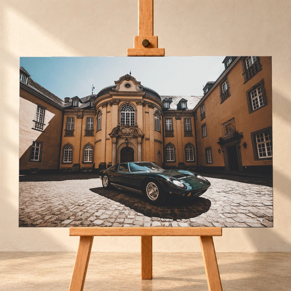 Visualisierung eines Leinwandbildes im Querformat, frontal auf einer Holzstaffelei vor heller Wand. Das Motiv zeigt einen dunkelgrünen klassischen Sportwagen auf Kopfsteinpflaster vor einer ockerfarbenen Barockfassade.