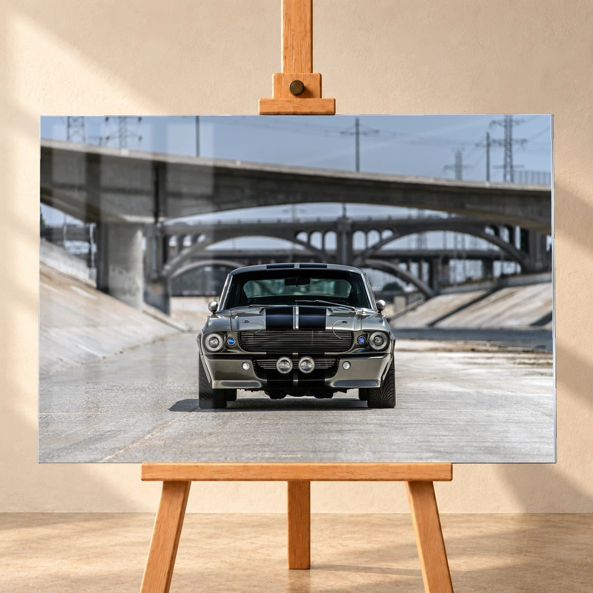 Als Acrylglas-Wandbild visualisiertes Eleanor-Motiv, frontal auf einer Holzstaffelei vor heller Wand präsentiert. Der silbergraue Ford Mustang Shelby GT500 mit schwarzen Doppelstreifen steht mittig in einem Betonkanal; dahinter liegen mehrere Brücken.