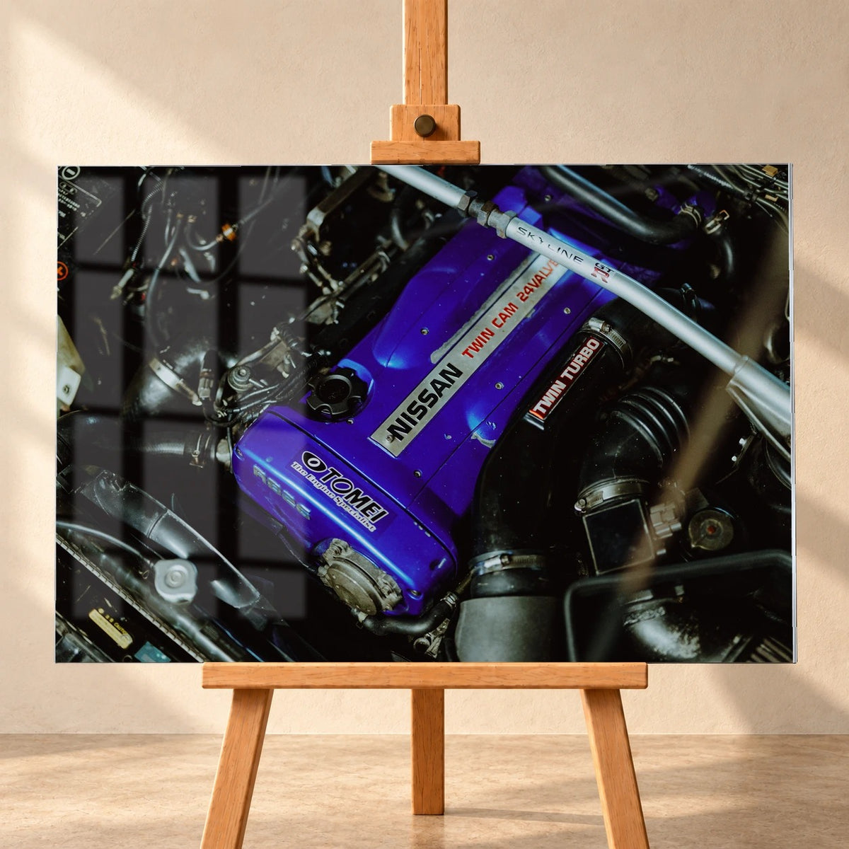 Frontalansicht eines Acrylglasbilds als Visualisierung auf einer Holzstaffelei vor heller Wand. Dargestellte Fensterreflexionen überlagern links das Motorraummotiv eines Nissan Skyline R33 mit violettem Ventildeckel und silberner Domstrebe.