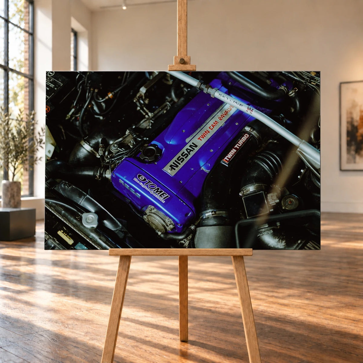 Raumvisualisierung mit einem querformatigen Leinwandbild auf einer Holzstaffelei in einem hellen Raum mit hohen Fenstern und Holzboden. Zu sehen ist der Motorraum eines Nissan Skyline R33 mit violettem Ventildeckel und silberner Domstrebe.