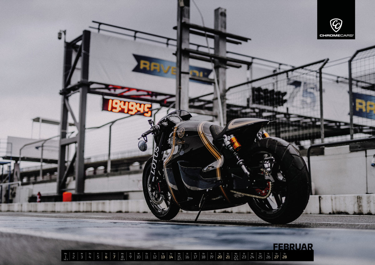 Black & Gold Collection Kalender 2027 – Februar: Das Lotus C-01 Motorrad steht seitlich in der Boxengasse vor Tribünen und Zeitnahme; die ungewöhnliche Silhouette wirkt wie ein Einzelstück