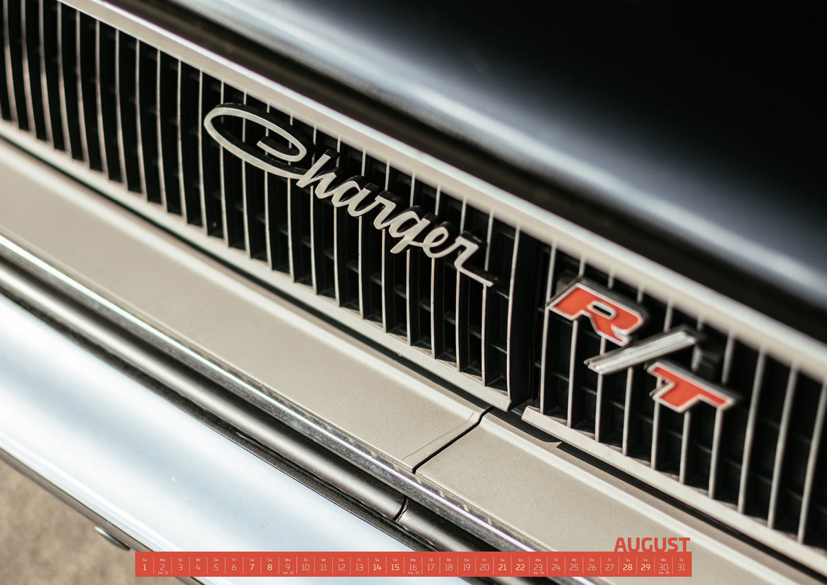 Bullitt Kalender 2027 – August: Diagonale Nahaufnahme eines hell lackierten Charger R/T mit schwarzem Lamellengrill, verchromtem Charger-Schriftzug und rot-weißem R/T-Emblem; Chromleisten reflektieren helles Licht