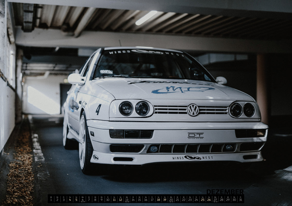 Jesse’s Jetta Kalender 2027 – Dezember: Weißer VW Jetta in tiefer, leicht seitlicher Frontansicht in einer dunklen Parkgarage. Vier runde Scheinwerfer, weiße Räder, Karosseriegrafiken und die Nummer 4 sind sichtbar; links…