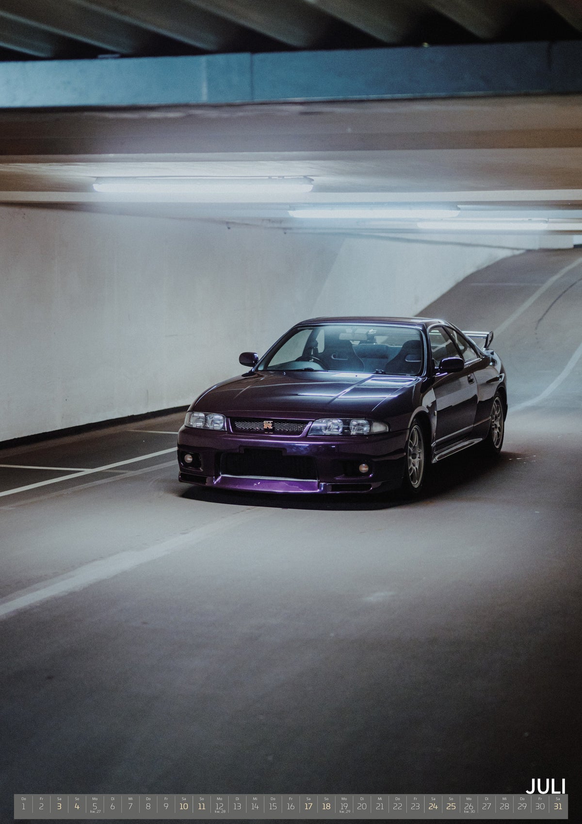 Midnight Purple I Kalender 2027 – Juli: Der Nissan Skyline R33 steht sehr weit hinten in einem hohen, schmalen Parkhaustunnel; die Bildtiefe dominiert das Motiv