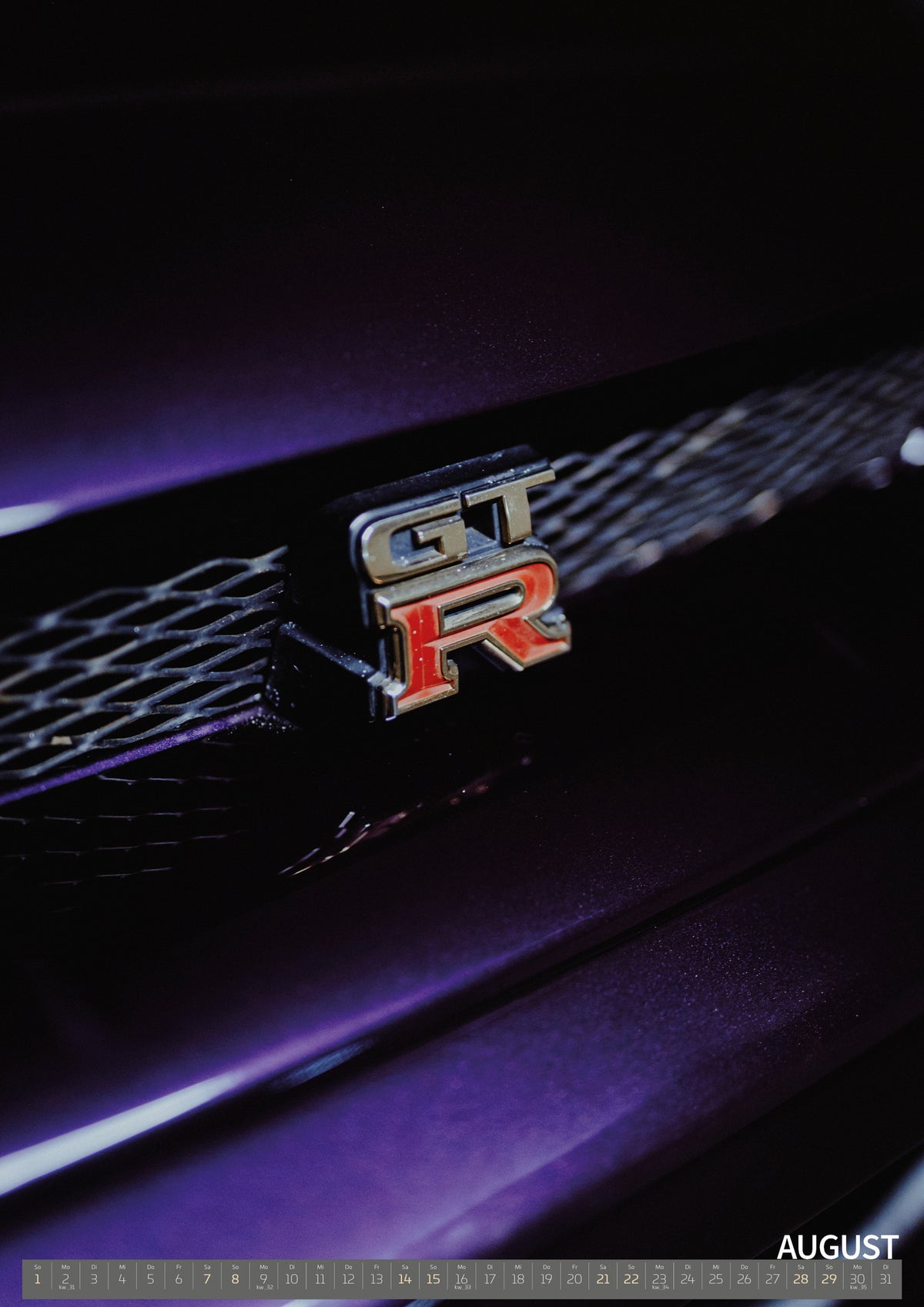 Midnight Purple I Kalender 2027 – August: Nahaufnahme eines rot-silbernen GT-R-Emblems an einem dunklen Frontgrill, beleuchtet von violettem Licht und umgeben von tiefen Schatten
