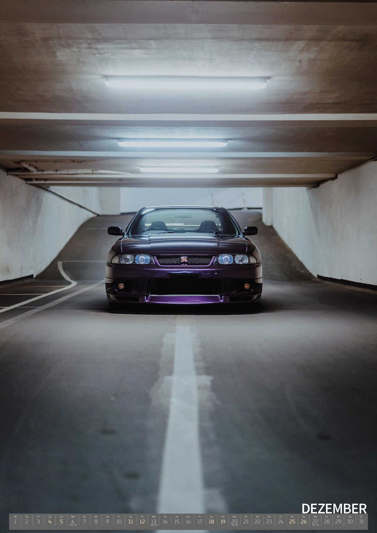Midnight Purple I Kalender 2027 – Dezember: Der Nissan Skyline R33 steht weit hinten exakt auf der Mittellinie eines leeren Parkhauses; die langen Deckenbalken verstärken die Tiefe