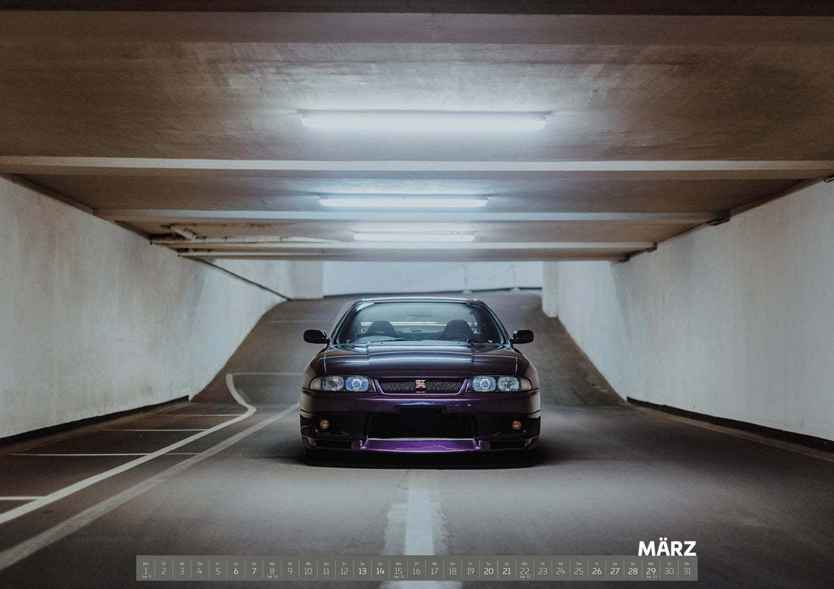 Midnight Purple I Kalender 2027 – März: Der Nissan Skyline R33 steht frontal auf der weißen Mittellinie eines leeren Parkhauses; die Deckenlichter bilden eine symmetrische Flucht