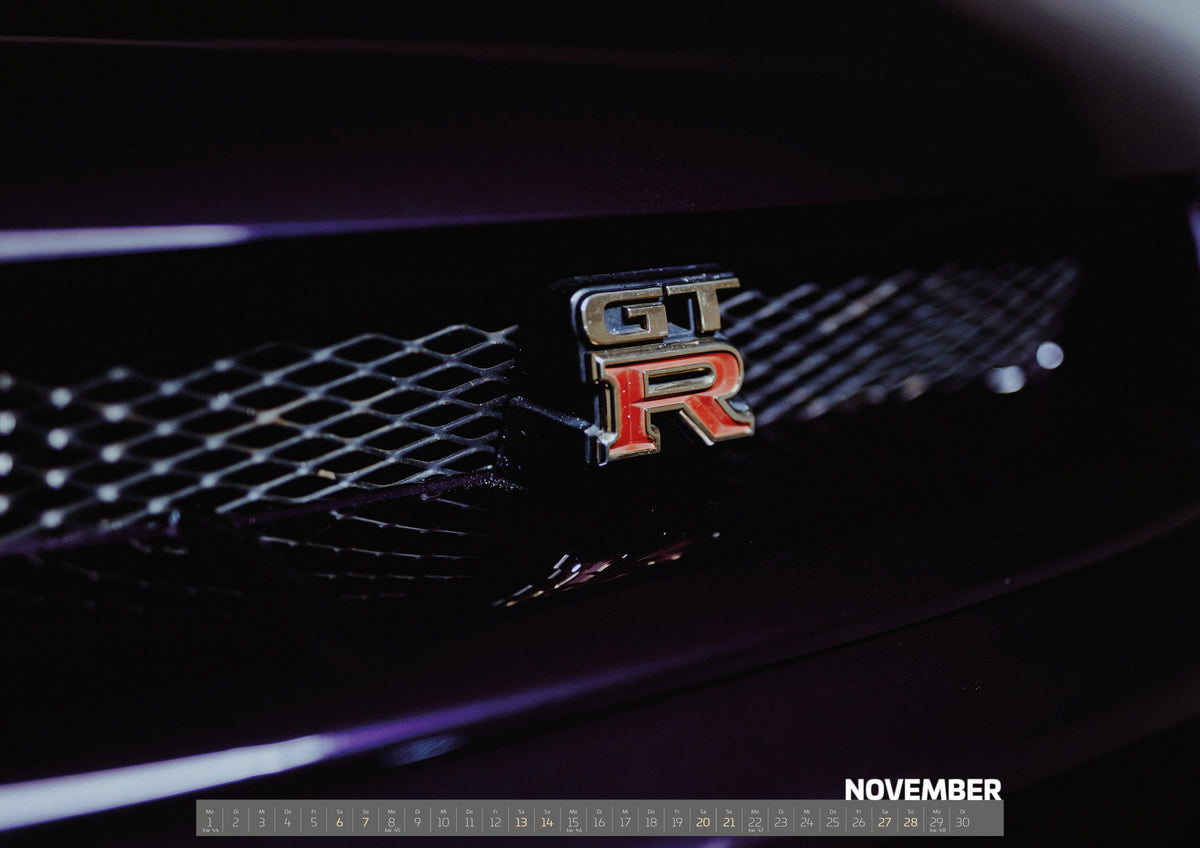 Midnight Purple I Kalender 2027 – November: Das rote GT-R-Emblem sitzt im schwarzen Kühlergrill; die enge Aufnahme macht Schriftzug und Gitterstruktur zum Motiv