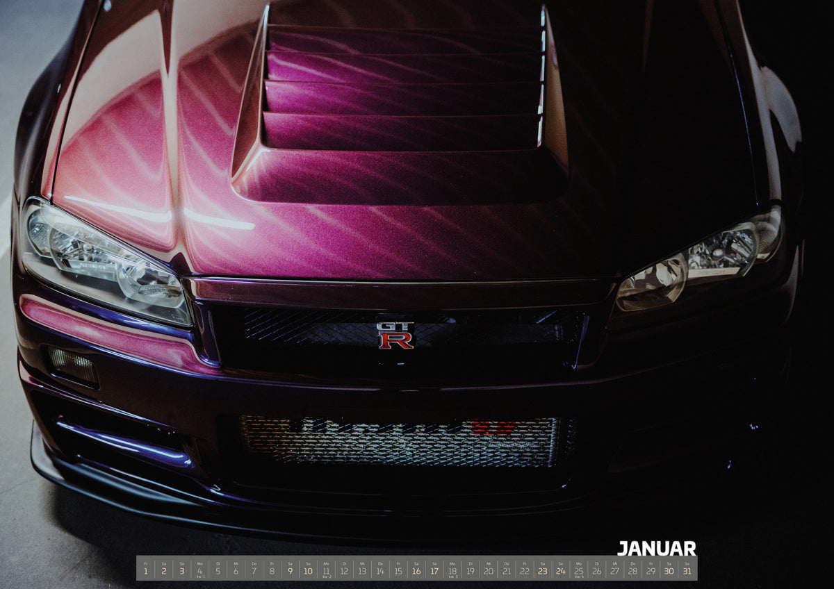 Midnight Purple Collection Kalender 2027 – Januar: Enge Frontansicht eines dunkelvioletten Nissan Skyline R34 mit sichtbarem GT-R-Emblem, Haubenöffnungen und Scheinwerfern; magentafarbenes Licht links, tiefer Schatten rechts