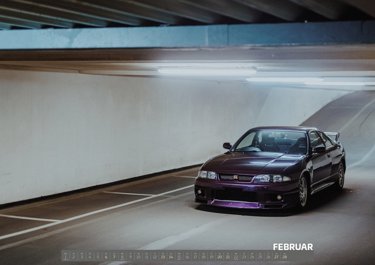 Midnight Purple Collection Kalender 2027 – Februar: Der Nissan Skyline R33 ist schräg von vorn zwischen Betonstützen aufgenommen; violette Lackreflexe und kühles Deckenlicht bestimmen die Szene