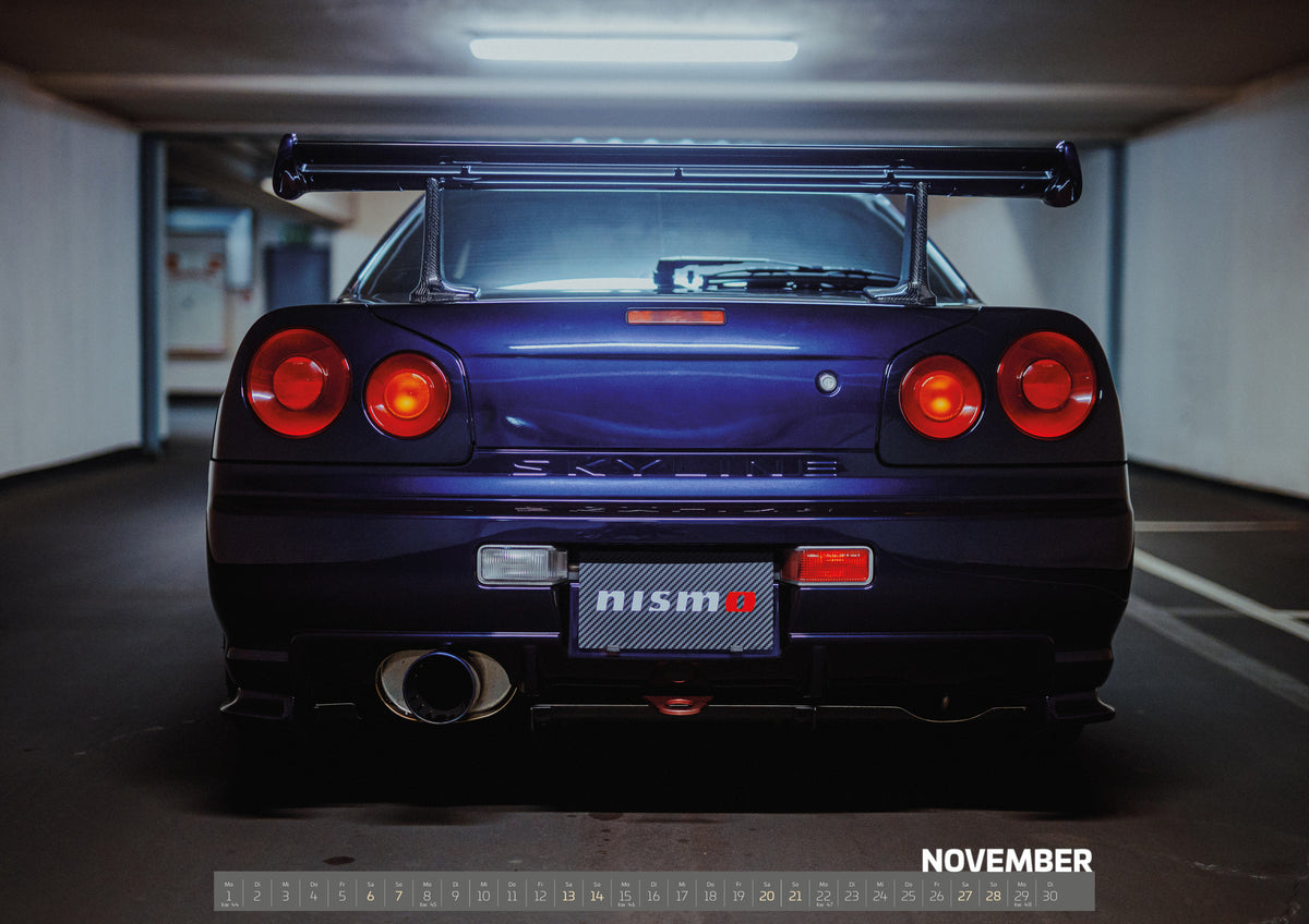 Midnight Purple Collection Kalender 2027 – November: Zentrierte Heckansicht eines dunkelvioletten Nissan Skyline R34 in einer Parkgarage. Sichtbar sind vier runde rote Rückleuchten mit orangefarbenen inneren Leuchtelementen, ein großer…
