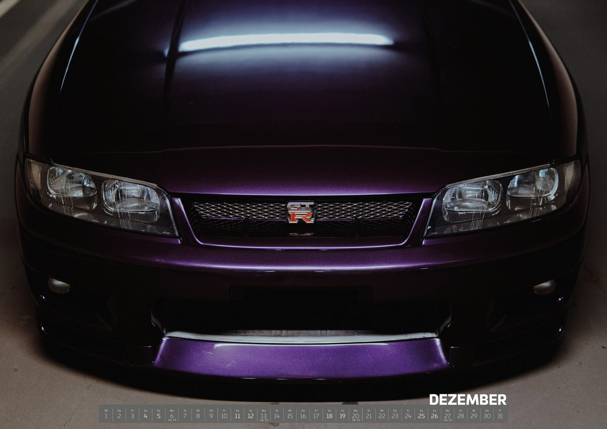 Midnight Purple Collection Kalender 2027 – Dezember: Eine enge Frontalansicht zeigt Grill, GT-R-Emblem und den violetten Frontsplitter des Nissan Skyline R33 vor dunklem Parkhausboden
