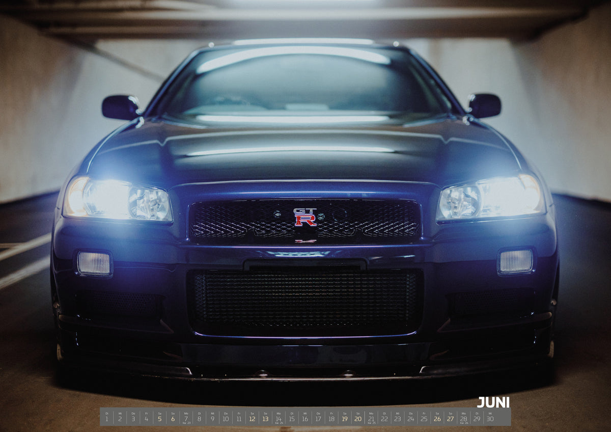 R34 Midnight Purple II Kalender 2027 – Juni: Der Nissan Skyline R34 füllt die Aufnahme frontal; helle Scheinwerfer, GT-R-Grill und violette Frontkante treten aus dem dunklen Umfeld hervor