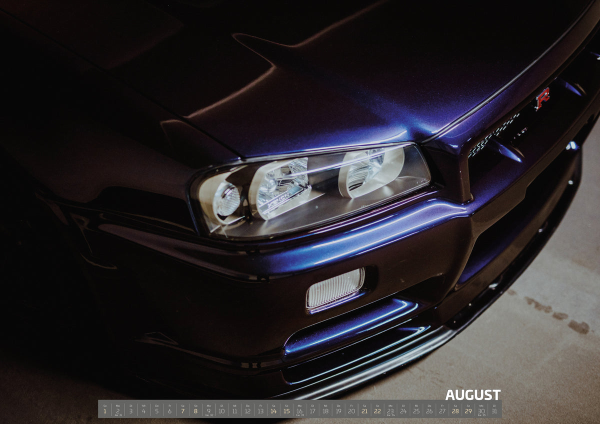 R34 Midnight Purple II Kalender 2027 – August: Eine schräge Nahaufnahme zeigt Scheinwerfer, Frontschürze und violette Lackkante des Nissan Skyline R34 unter hartem Neonlicht