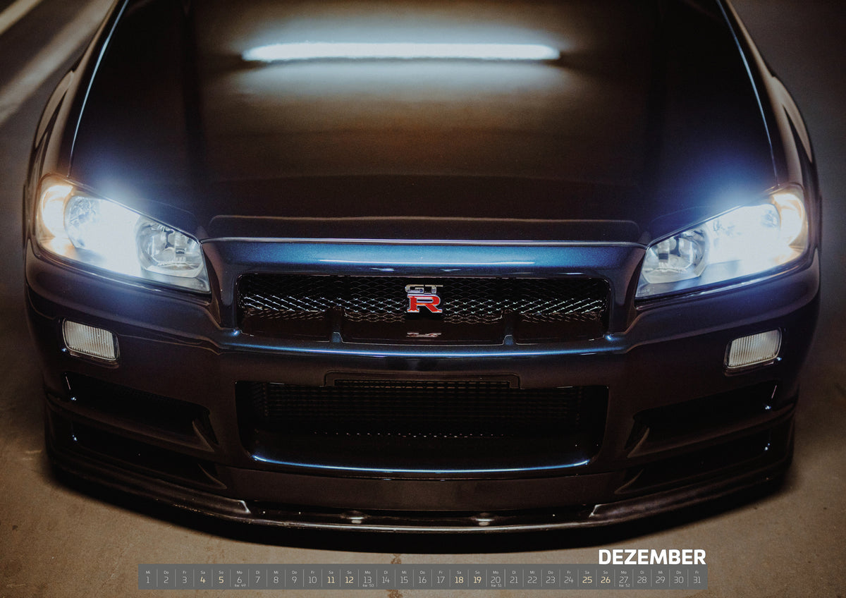 R34 Midnight Purple II Kalender 2027 – Dezember: Die breite Front des Nissan Skyline R34 füllt das Bild; beide Scheinwerfer leuchten über dem dunklen Stoßfänger