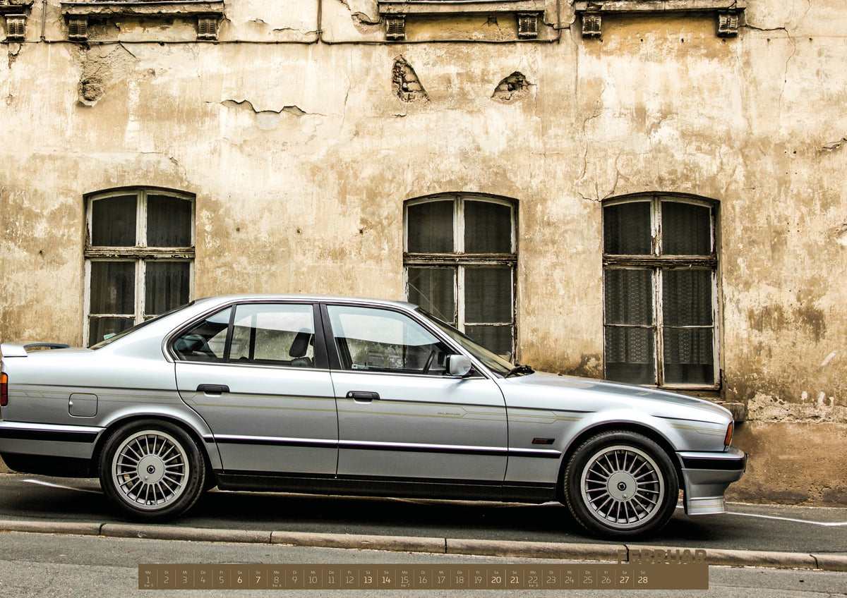 ChromeCars Retrospektiv II Kalender 2027 – Februar: Der silberne BMW Alpina B10 steht exakt im Seitenprofil vor einer verwitterten hellen Fassade; klare Linien und klassische Felgen dominieren