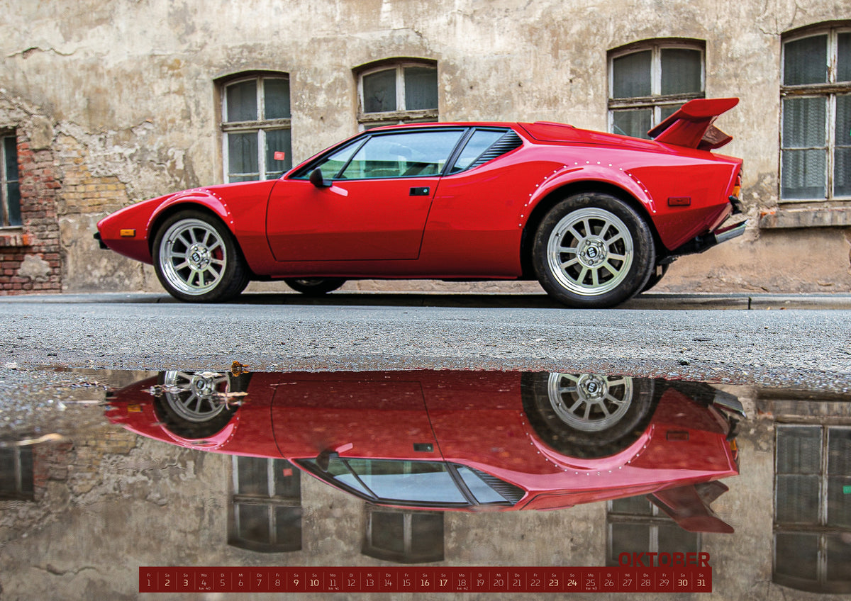 ChromeCars Retrospektiv II Kalender 2027 – Oktober: Der rote De Tomaso Pantera steht seitlich vor einer alten Backsteinfassade; eine große Pfütze spiegelt das gesamte Fahrzeug