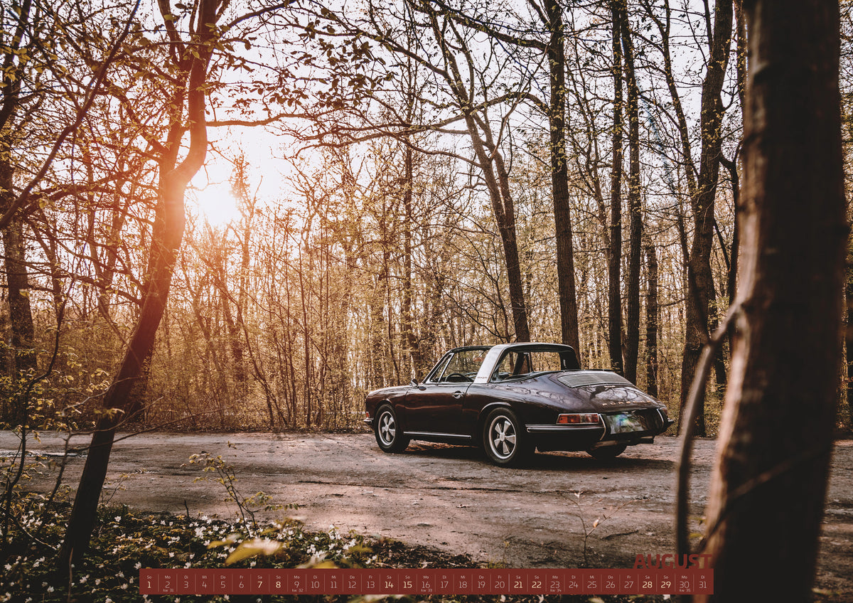 ChromeCars Retrospektiv Kalender 2027 – August: Dunkler 1967 Porsche 911 S Softwindow in seitlicher Heckansicht auf einer unbefestigten Fläche im Wald. Die offene Dachpartie und die helle Bügelzone sind sichtbar, während tiefes…
